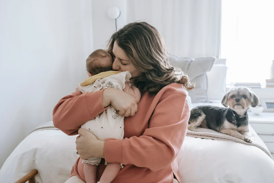 Mère assise sur un lit serrant son bébé contre elle dans une chambre claire