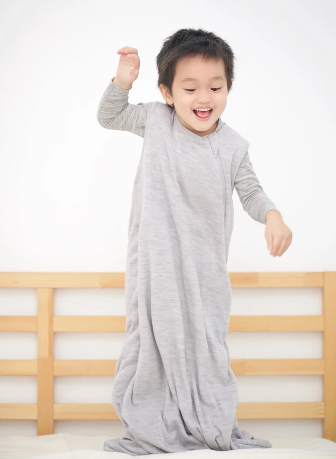 Enfant debout dans un sac de couchage gris à manches sur un lit