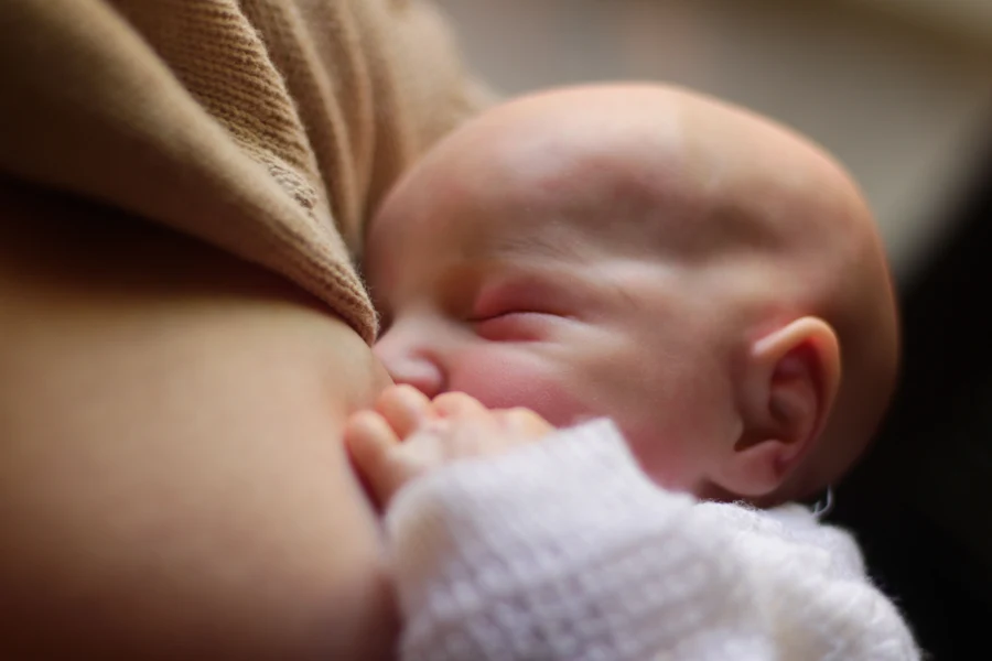 Mère allaitant son nouveau-né au sein, pull clair, lumière douce